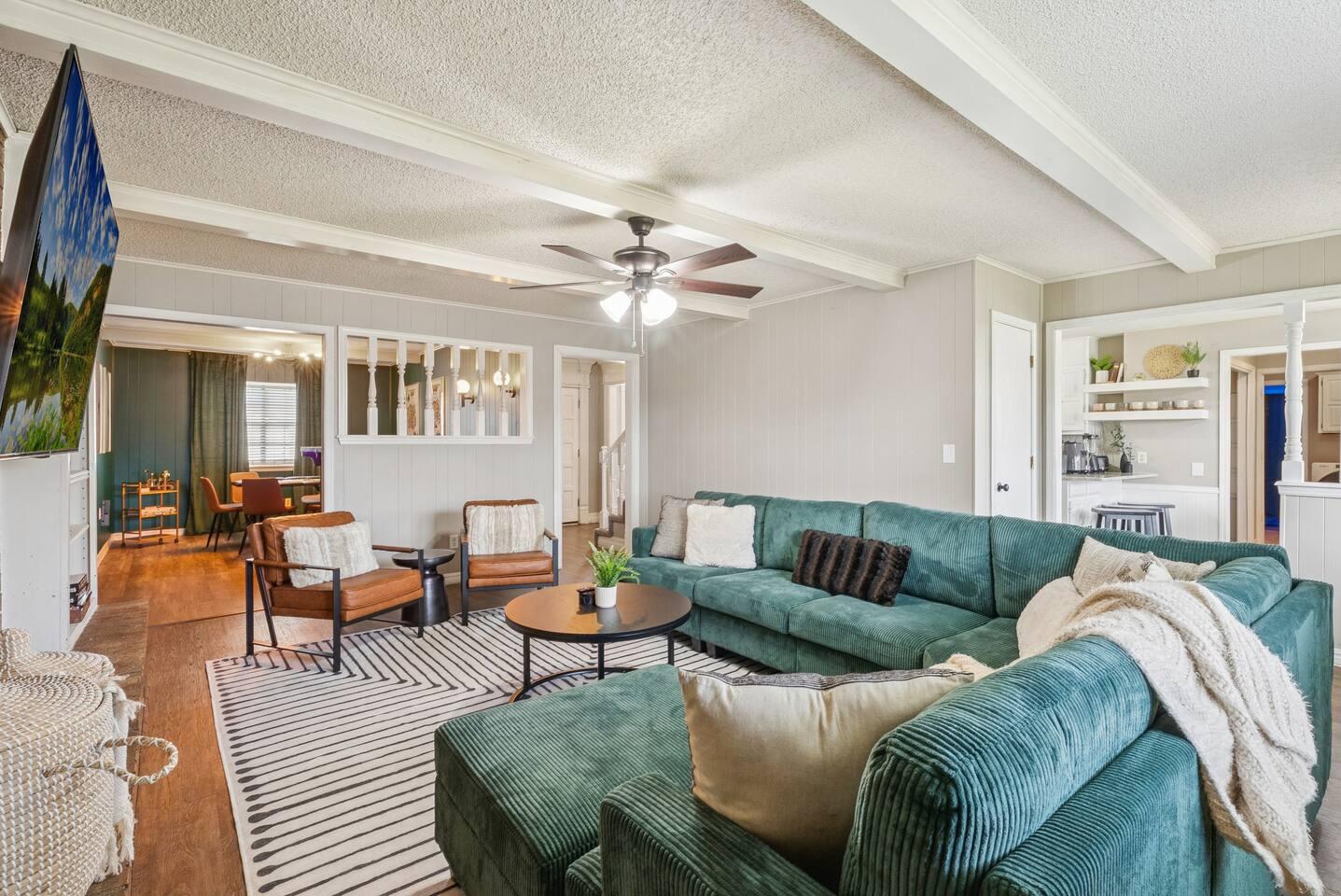 Living Room – Spacious layout with plush sectional, accent chairs, coffee table, ceiling fan, exposed beams, and open views to dining and kitchen areas.